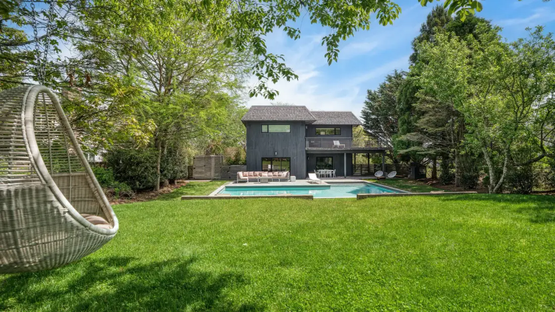 A modern house overlooks a swimming pool and broad green lawn.