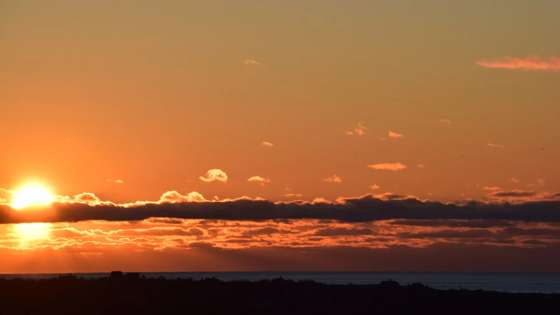 A sunset glows over a distant horizon and calm water.