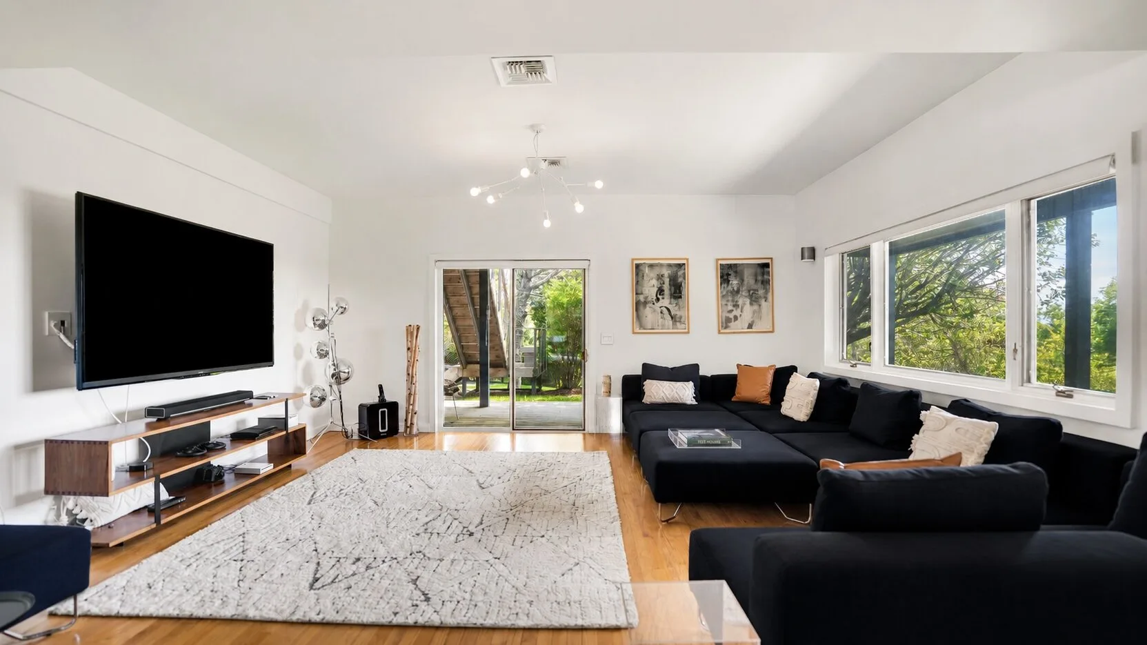 A bright living room with a large black sectional and wide windows.