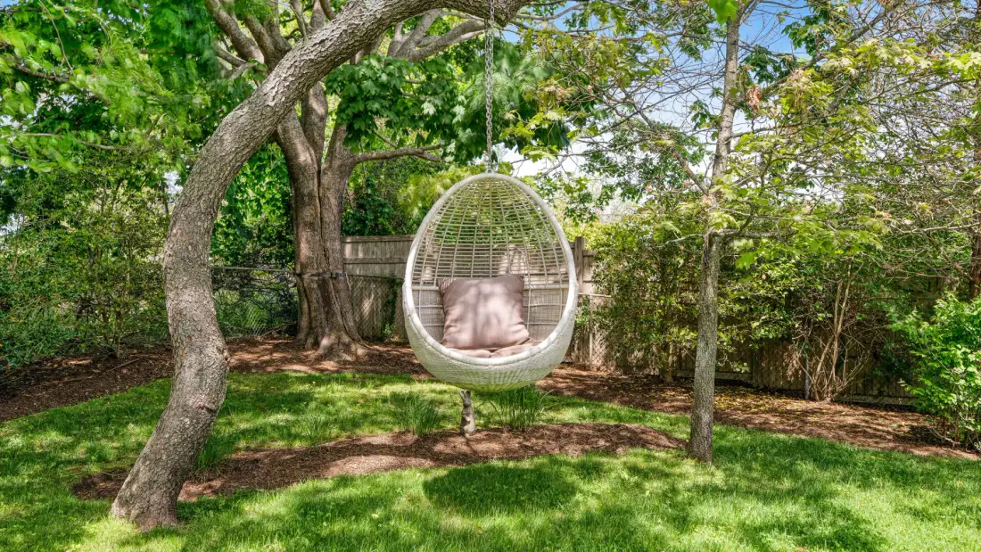 A leafy garden with a hanging egg chair beneath mature trees.