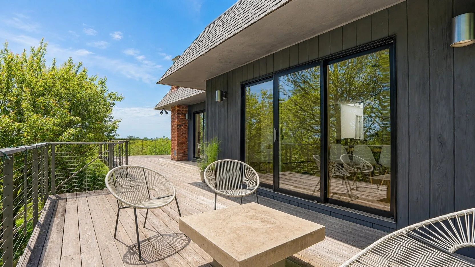 A sunny outdoor deck with seating beside large glass doors.