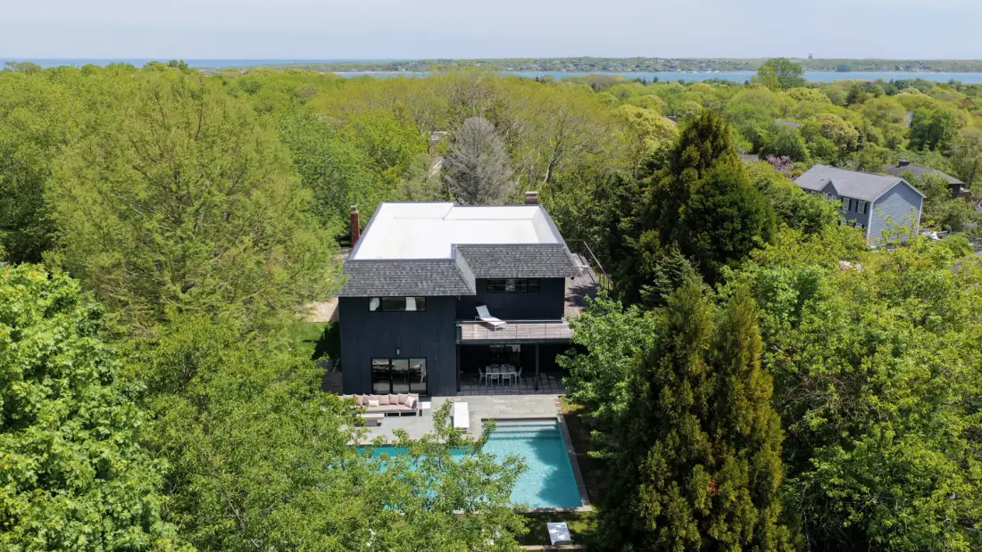 Aerial view of a modern house surrounded by dense greenery, with a swimming pool.