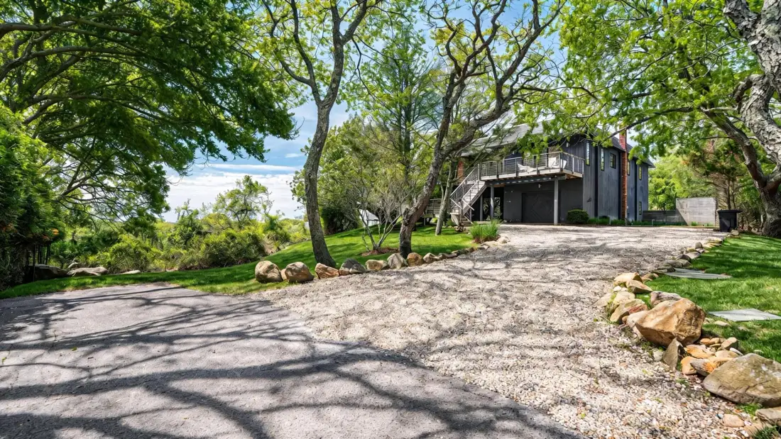 A gravel driveway leads through leafy trees to a modern house.