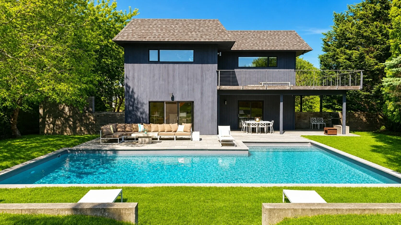 Una casa moderna junto a una piscina, rodeada de árboles y césped.
