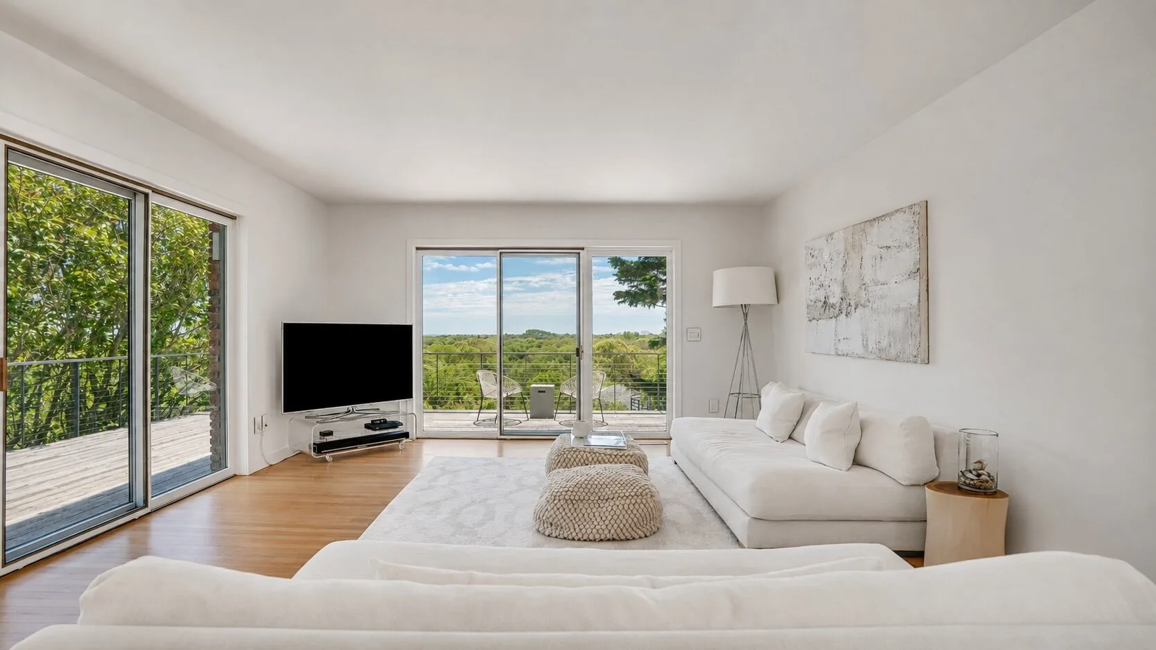 A bright living room with seating and large windows overlooking greenery.