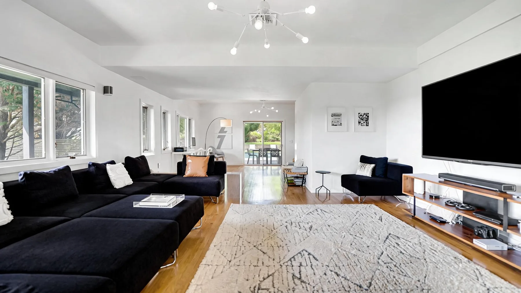 A bright living room with dark seating, a large rug, and a wall-mounted television.