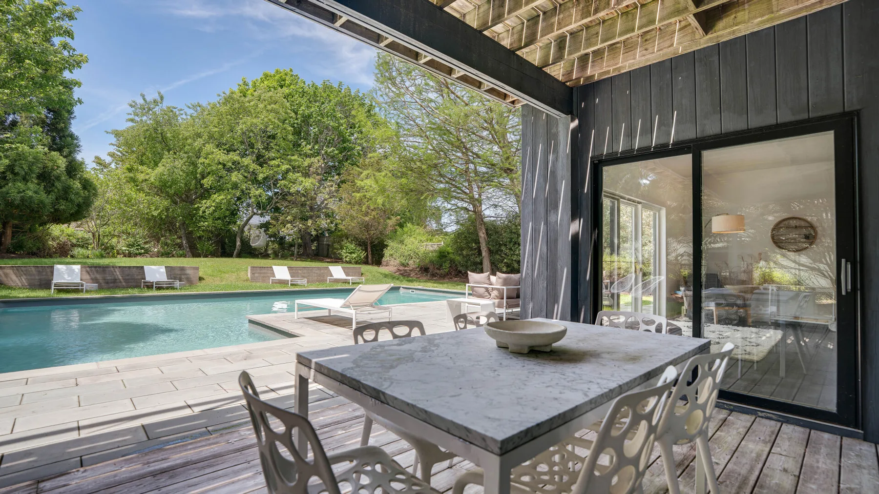 A covered patio dining area overlooks a swimming pool and leafy garden.