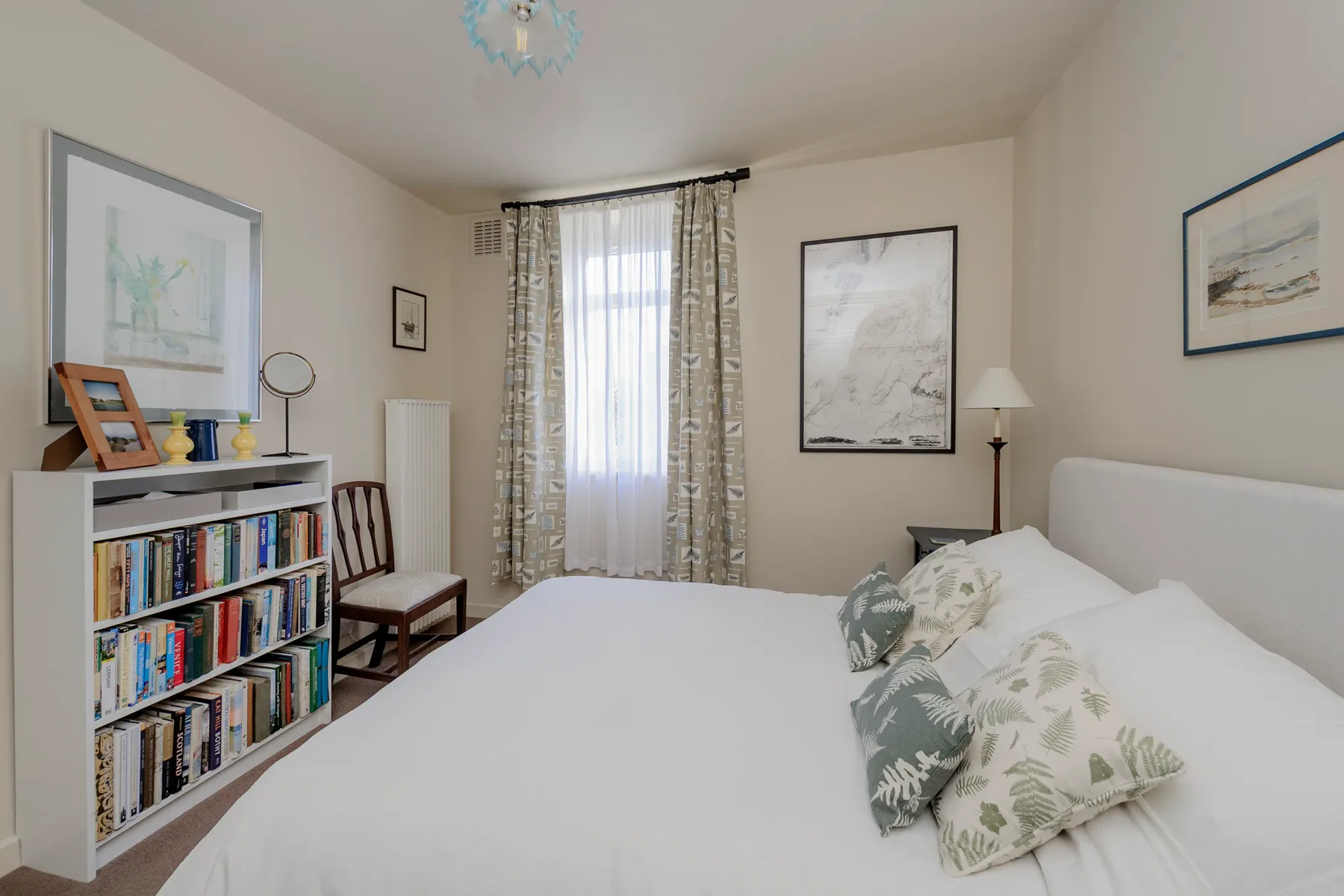 Un dormitorio luminoso con una cama, una estantería y una ventana con cortinas.