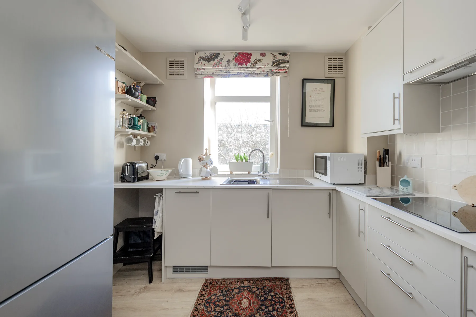 Una cocina luminosa con gabinetes blancos, una ventana y electrodomésticos sobre la encimera.