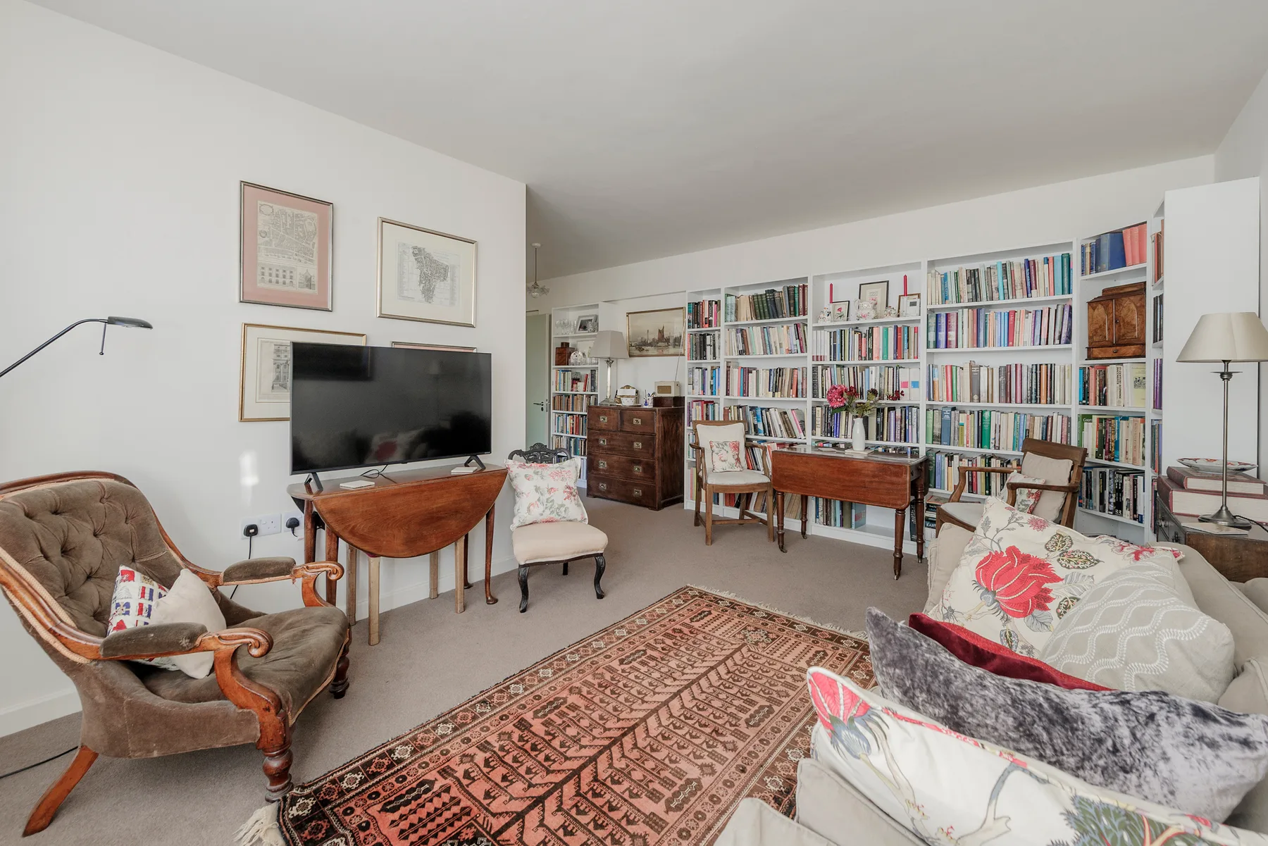 Una sala de estar con amplias estanterías de libros, asientos y una alfombra estampada.