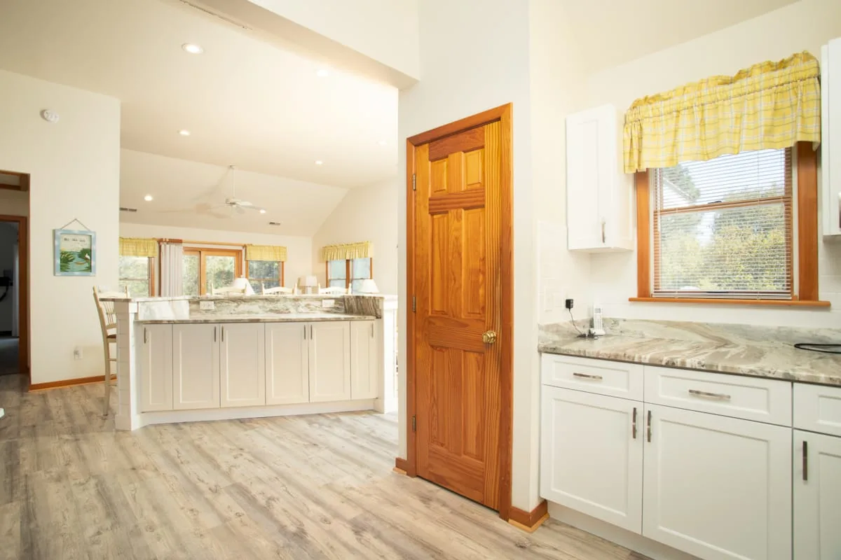 A bright kitchen with white cabinetry, a countertop island, and a wood door.