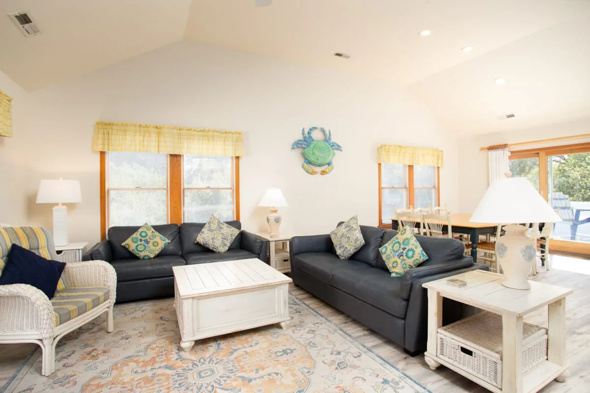 A bright living room with dark seating, a white coffee table, and large windows.