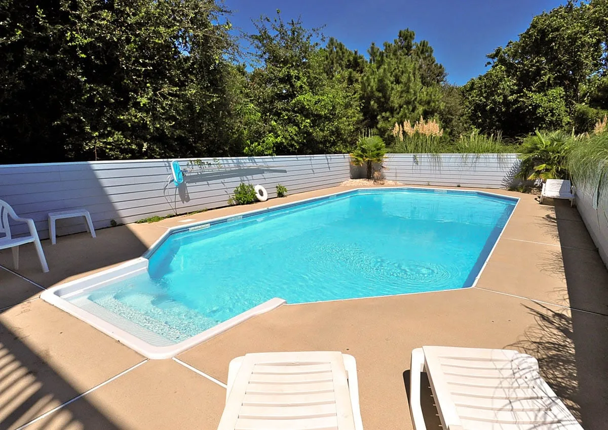 Una piscina al aire libre está rodeada de una terraza pavimentada y vegetación.