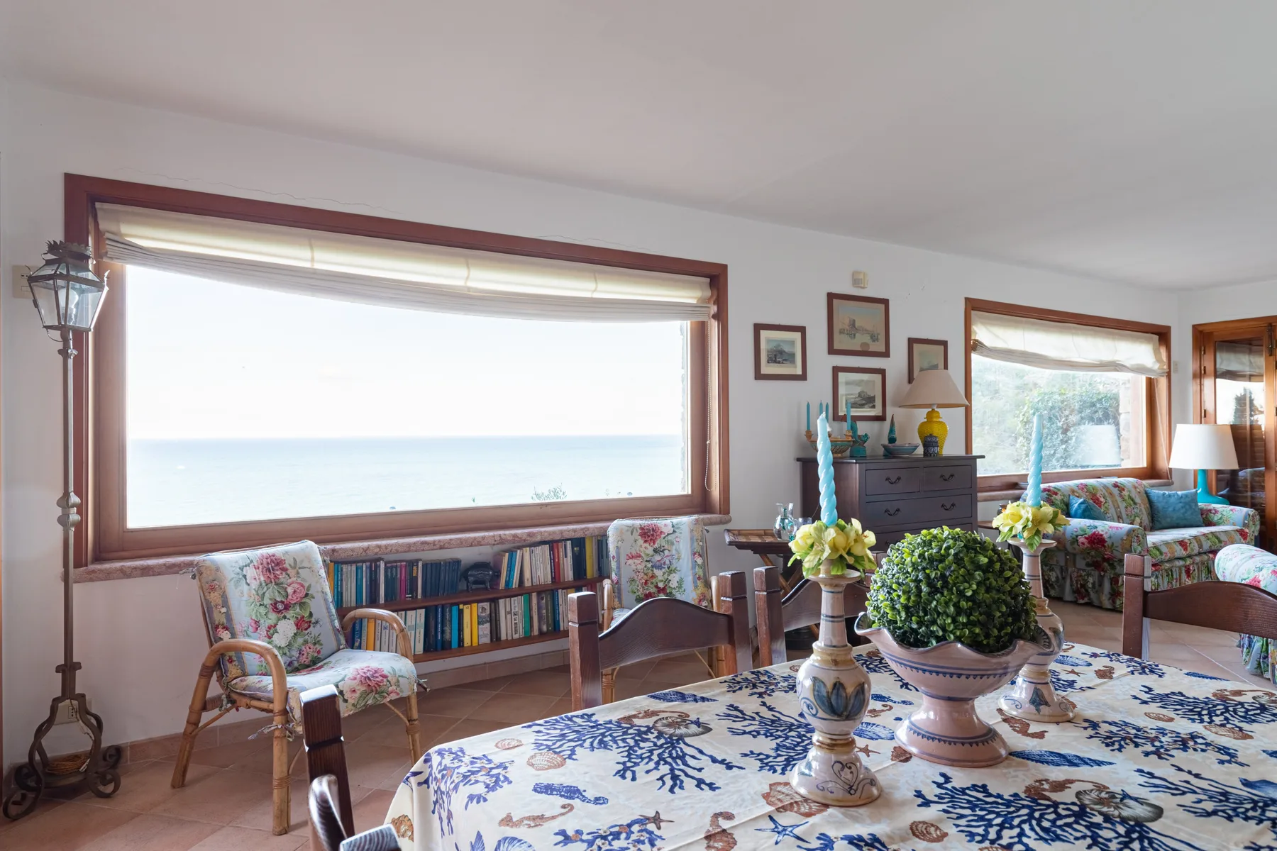 A bright living room with a large window overlooking the water and floral seating.