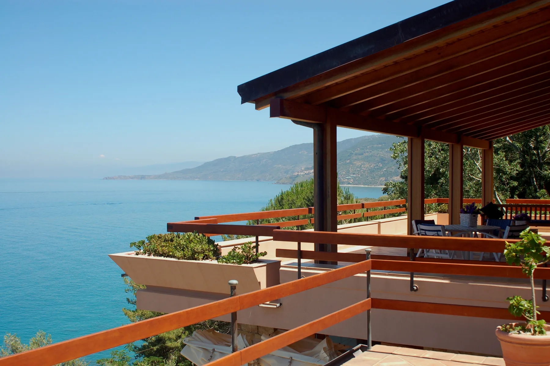 A covered outdoor terrace overlooks the blue sea and distant coastline.