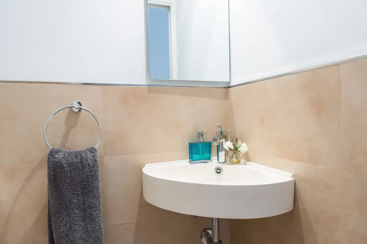 Un lavabo de baño con espejo, lavamanos blanco y aro para toalla.