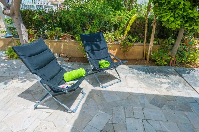 Dos asientos reclinables están en un patio pavimentado junto a un jardín frondoso.