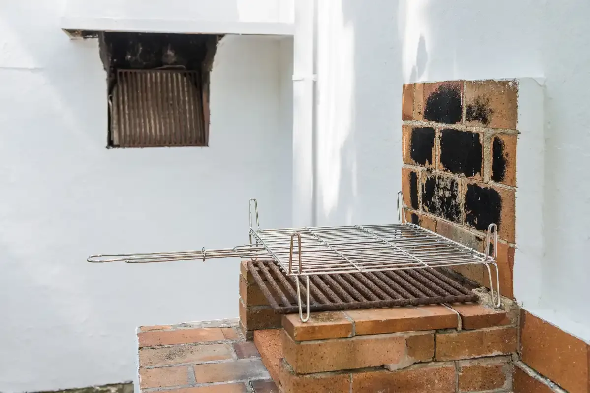 Una parrilla de ladrillo está junto a una pared blanca.