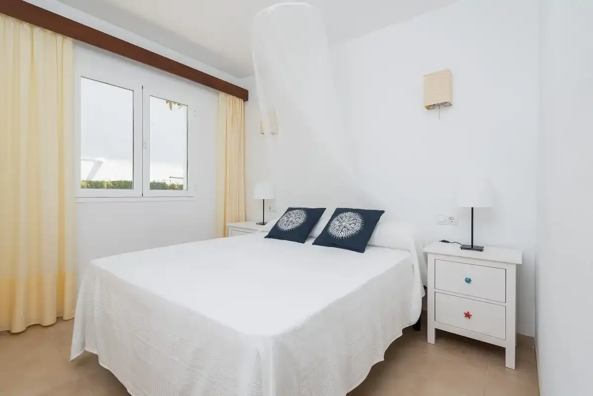 Un dormitorio con una cama bien hecha y una ventana con cortinas claras.