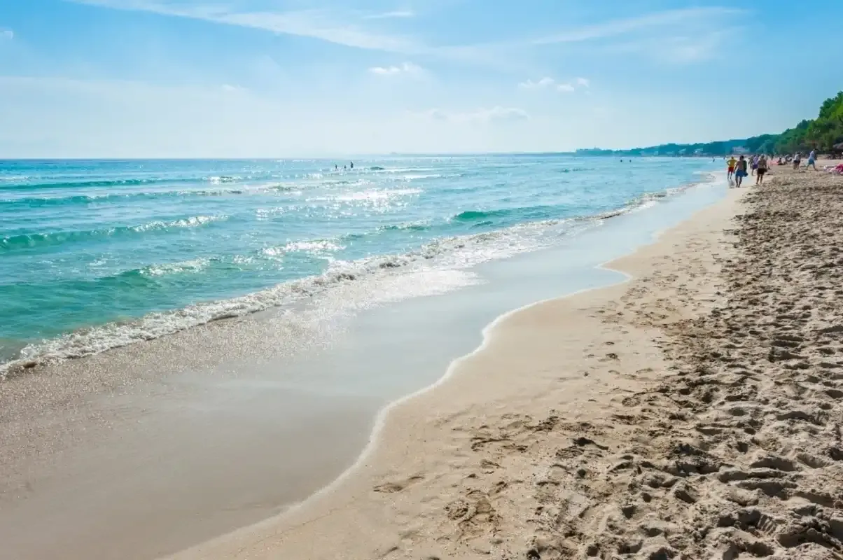 Una playa de arena se extiende junto a aguas azules bajo un cielo despejado.