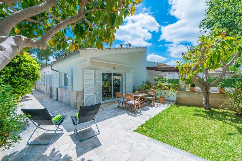 Un patio soleado con asientos al aire libre junto a una casa de color claro.