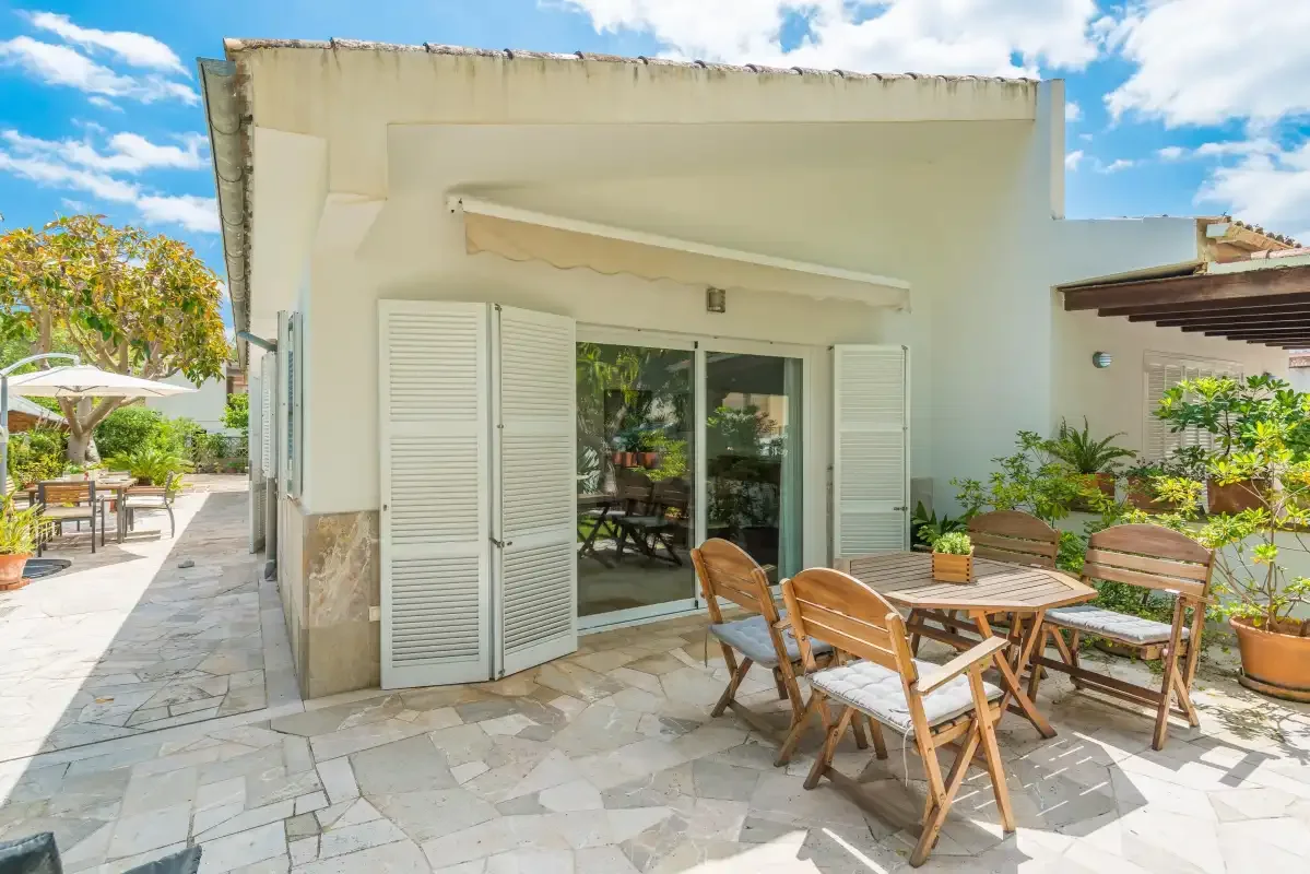 Un patio exterior luminoso con mesa de comedor y asientos junto a una puerta de cristal.