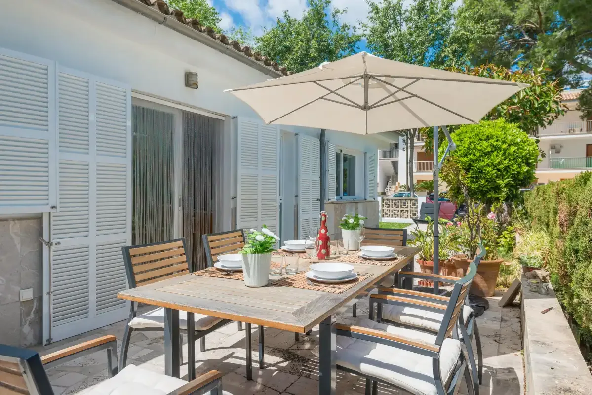 Comedor exterior con una mesa y una sombrilla junto a una casa blanca.