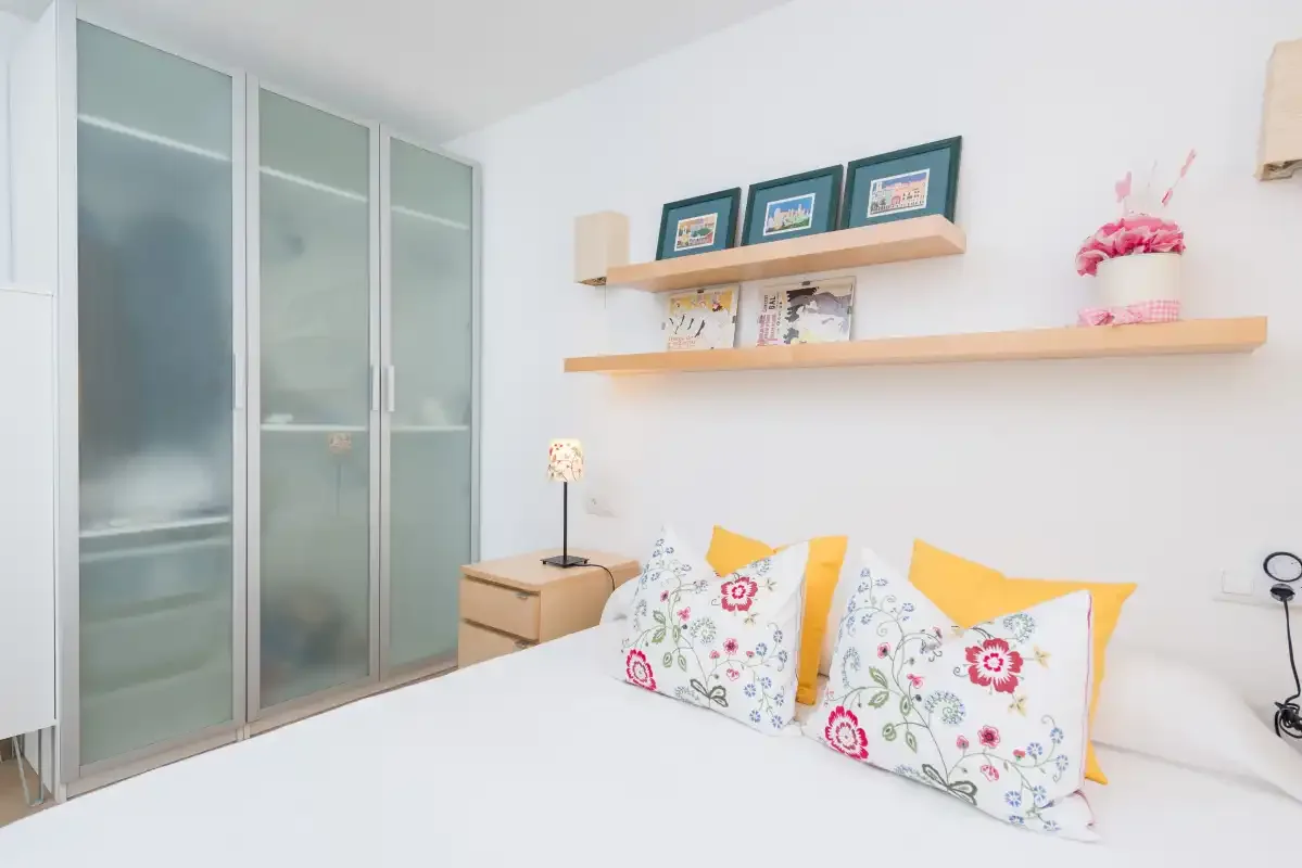 Un dormitorio luminoso con almohadas florales sobre la cama y armarios empotrados.