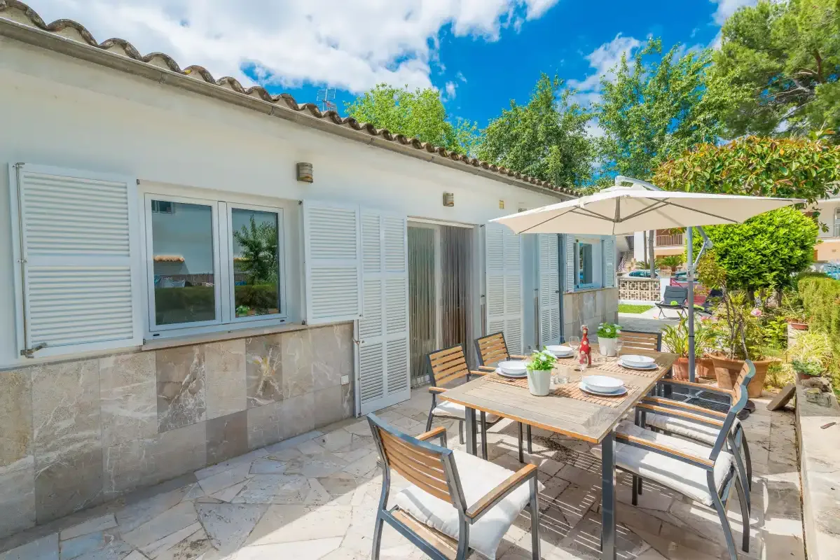Un patio soleado con asientos al aire libre y una sombrilla grande junto a una casa blanca.