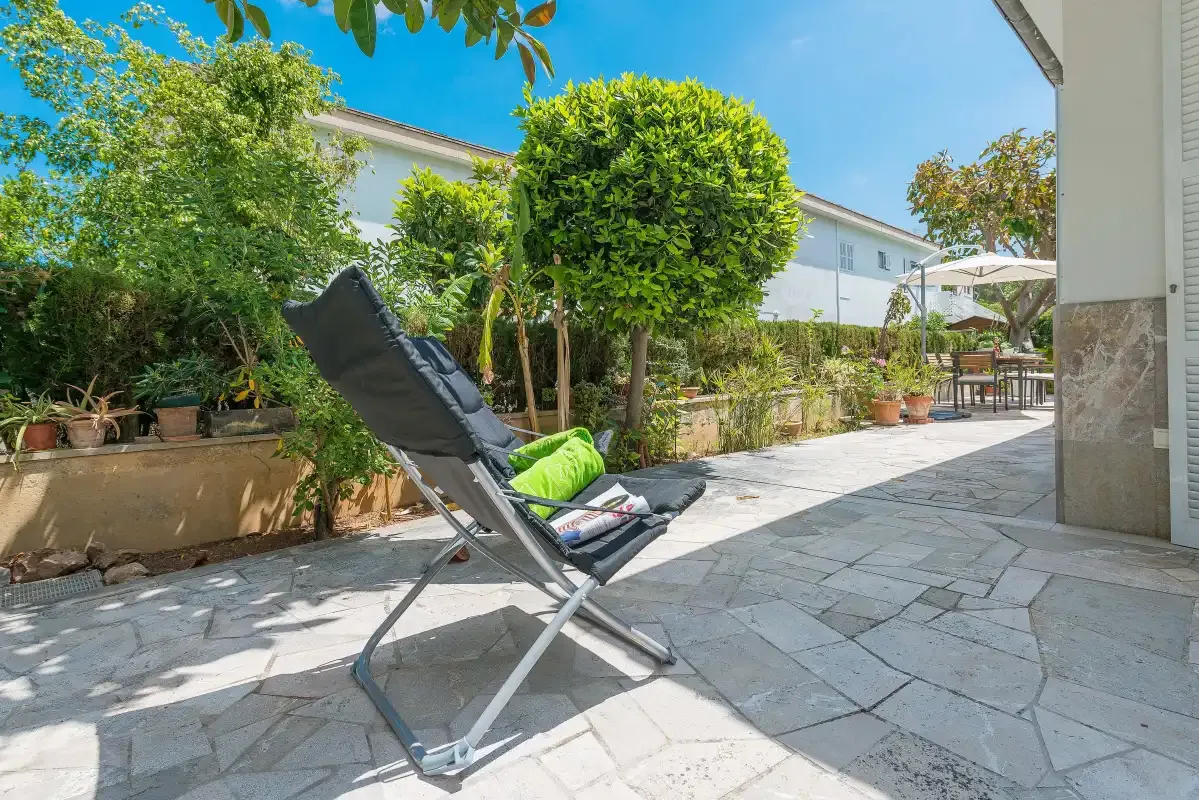 Un patio pavimentado con un asiento reclinable, plantas en macetas y vegetación frondosa.