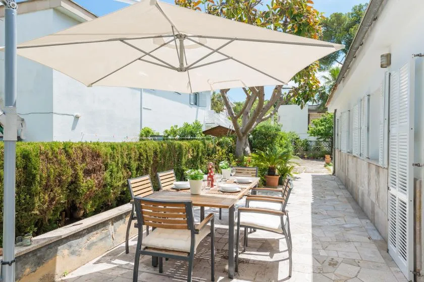 Un comedor al aire libre está bajo una sombrilla grande junto a un seto.