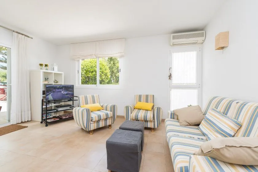 Una sala luminosa con asientos a rayas, un televisor y ventanas.