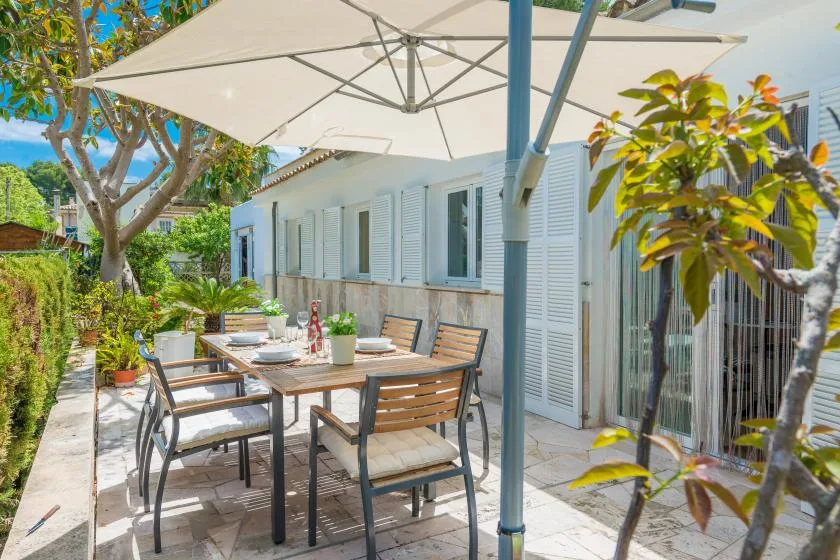 Un patio al aire libre con una mesa de comedor y sillas bajo una sombrilla grande.