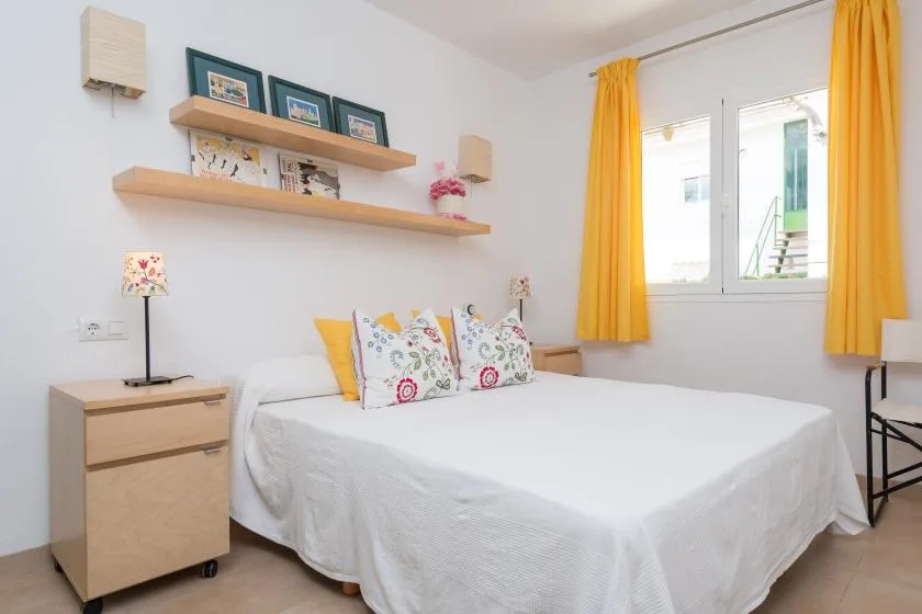 Un dormitorio luminoso con una cama bien hecha y cortinas amarillas junto a la ventana.