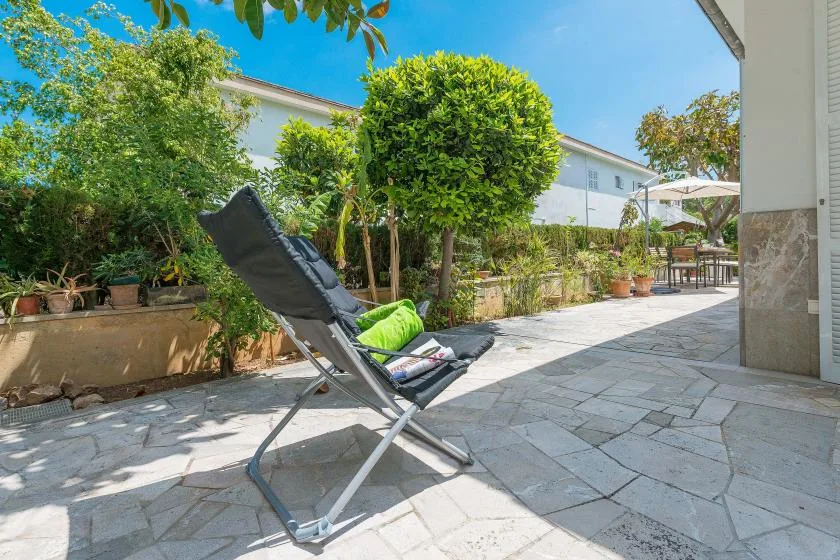 Un patio exterior pavimentado con una silla reclinable y plantas frondosas.