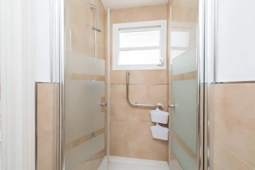 Una zona de ducha con azulejos, paneles de vidrio y una ventana pequeña.