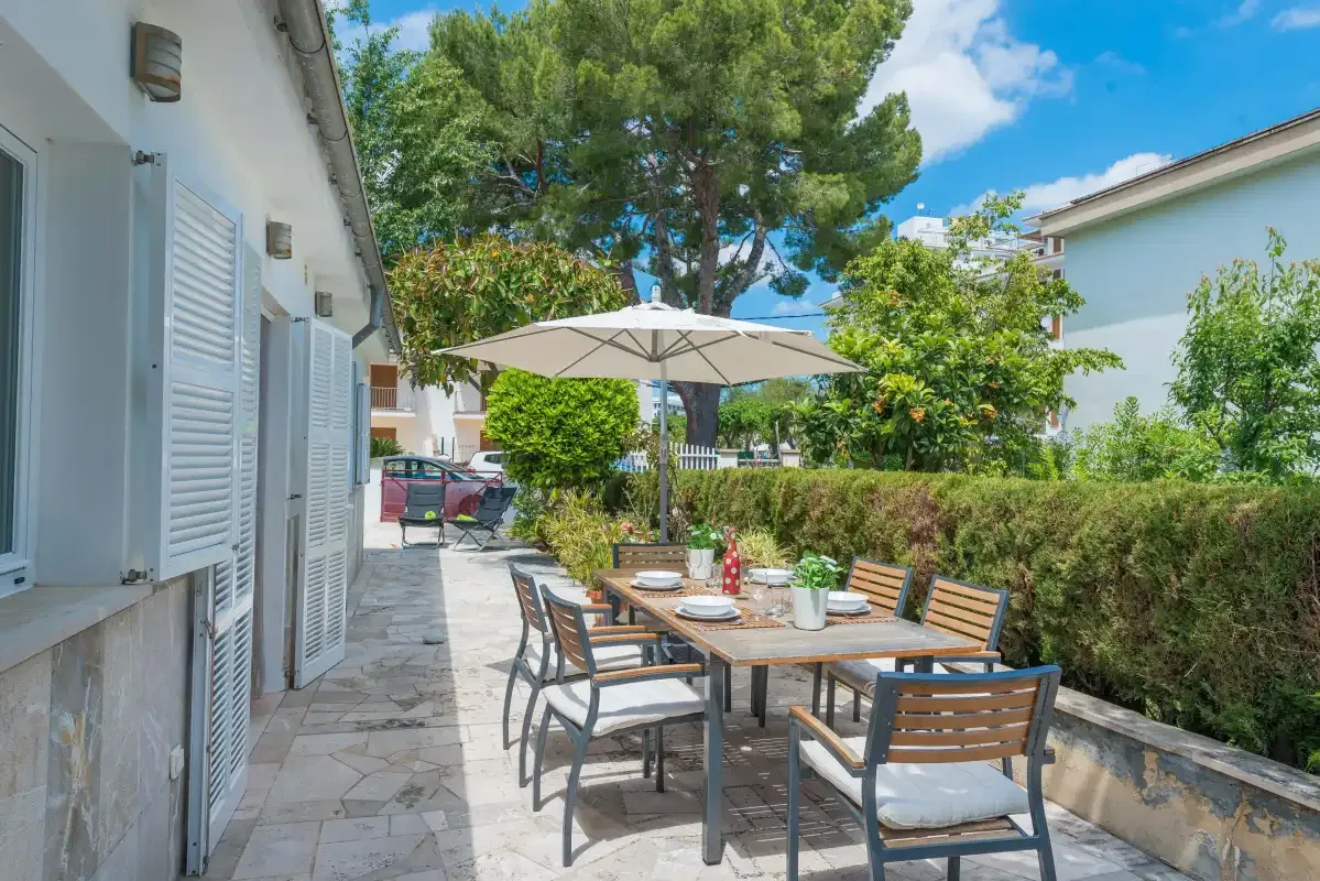 Un patio exterior con una mesa de comedor, asientos y una sombrilla grande.