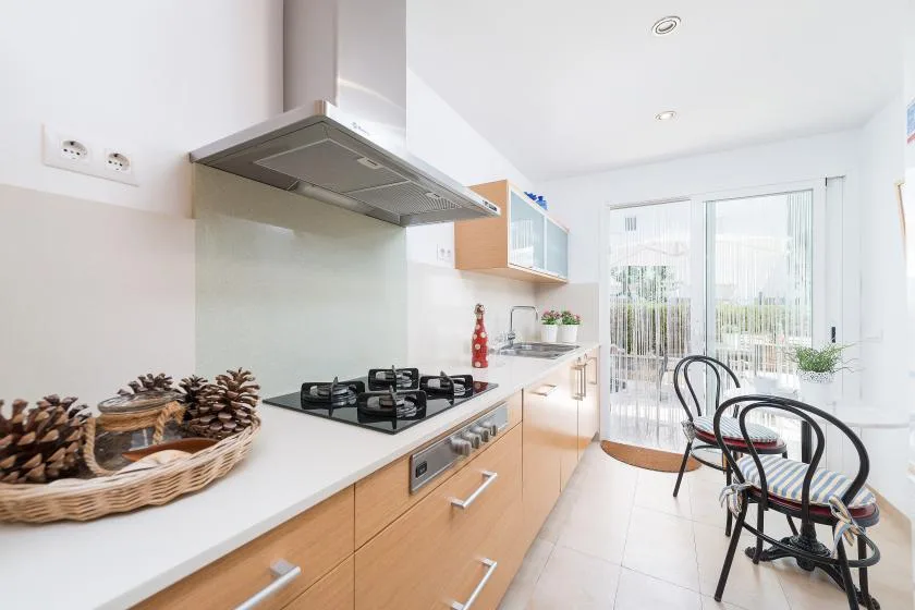 Una cocina luminosa con una placa de cocina y una pequeña mesa junto a puertas corredizas de vidrio.