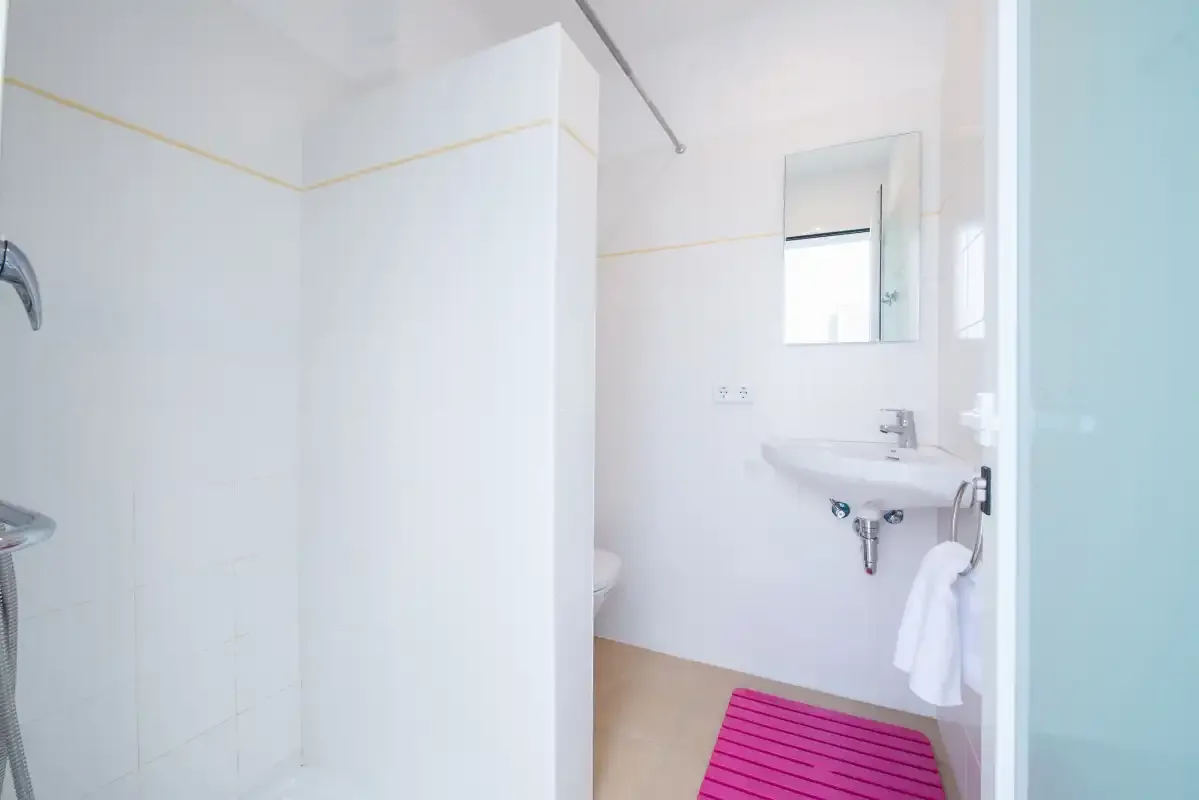 Un baño luminoso con lavabo, espejo y alfombrilla rosa.