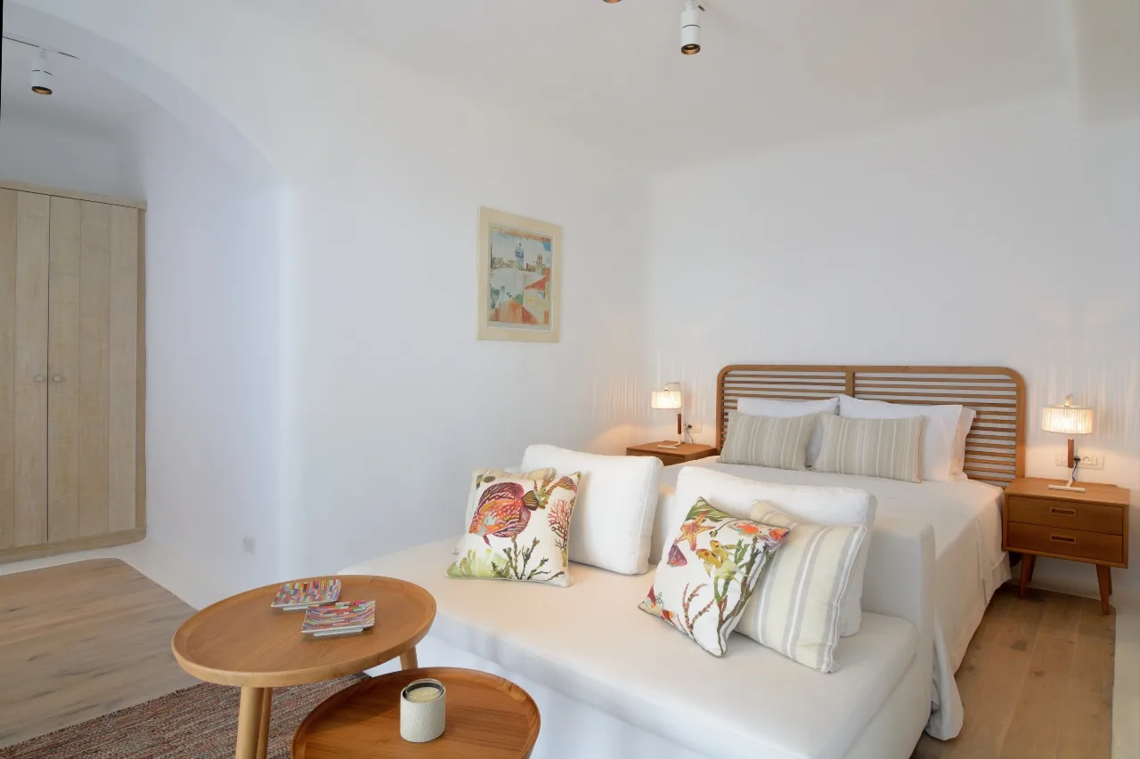 A bedroom with a bed, white seating, and wooden bedside tables.