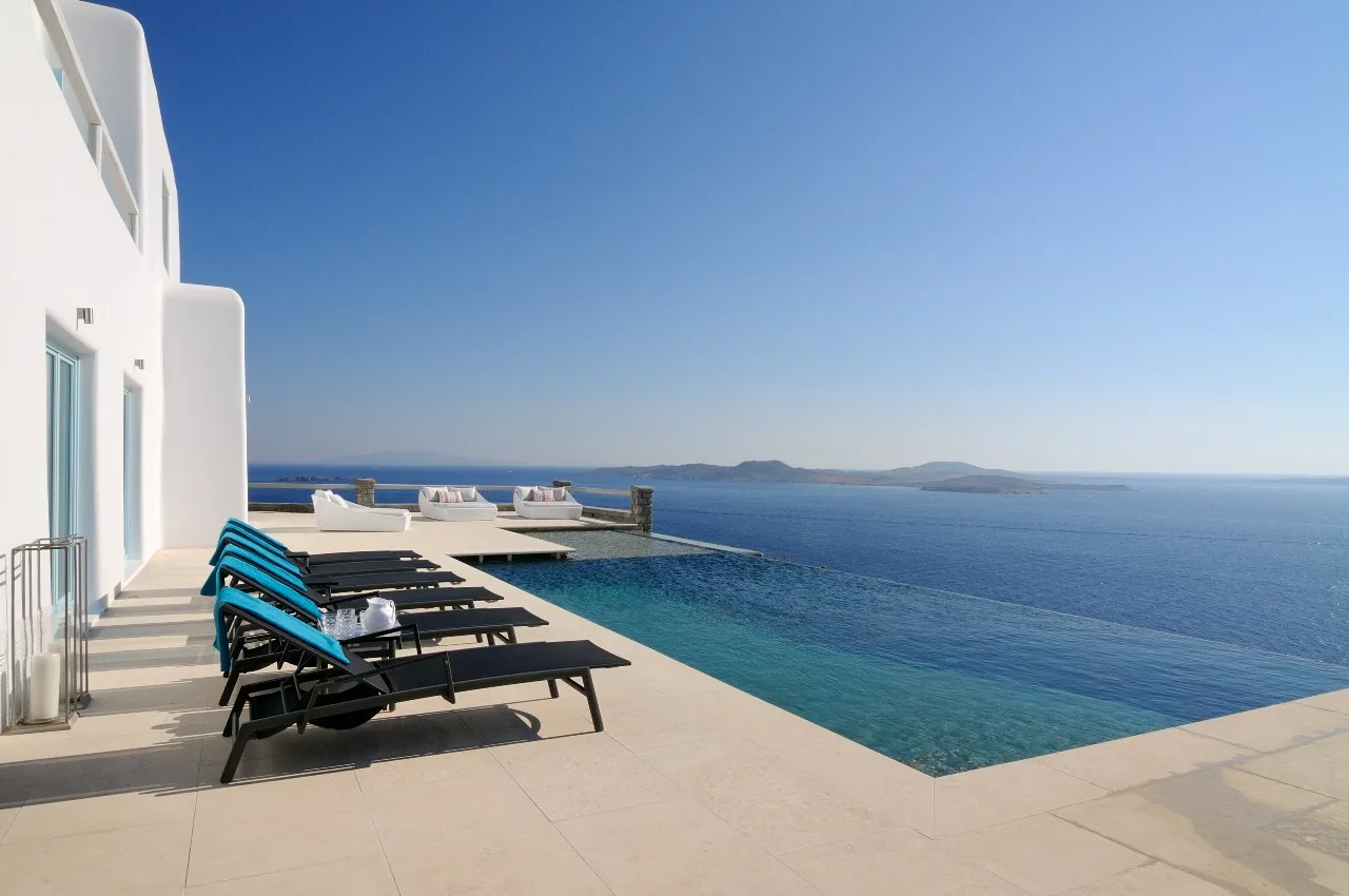 A poolside terrace with lounge seating overlooks the sea.