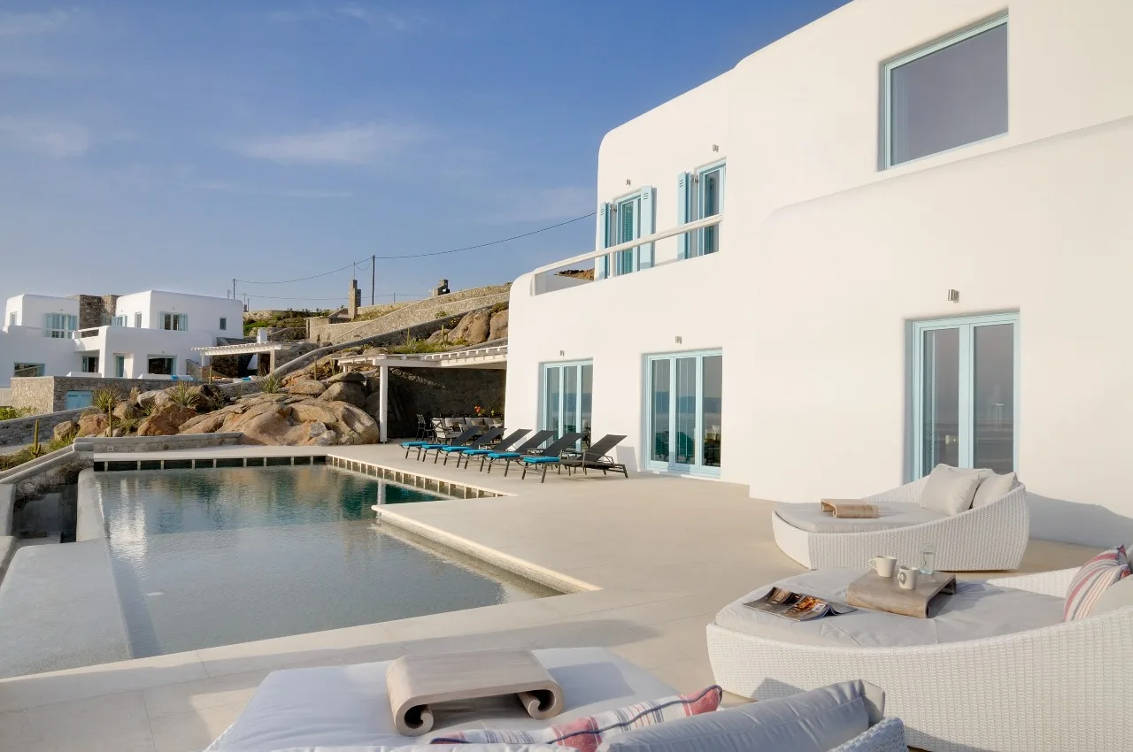 A modern white villa opens onto a pool and a sunlit terrace.