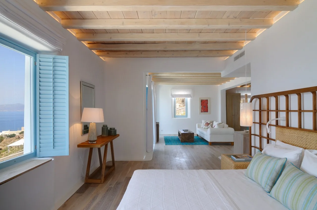 A bright bedroom opens onto a sitting area, with a large window overlooking the sea.