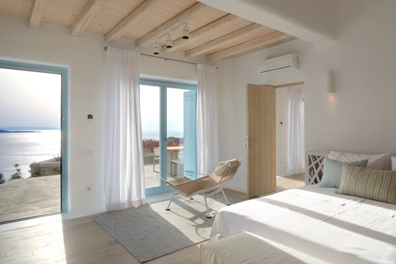A bright bedroom opens onto a balcony with a view of the sea.