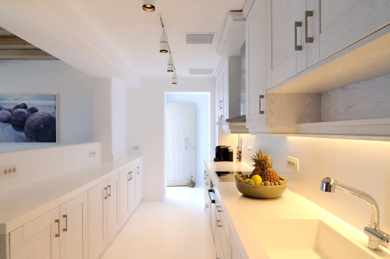 A bright galley kitchen with white cabinets and a bowl of fruit on the counter.