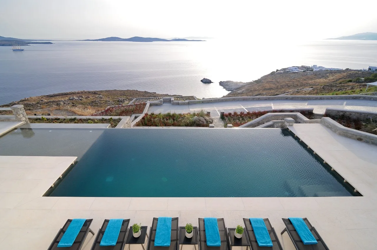 An outdoor pool overlooks the sea, with blue lounge chairs along the deck.