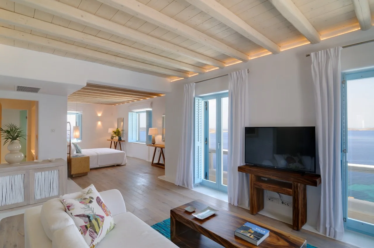 A bright living room with seating, a television, and tall windows opening onto a balcony.
