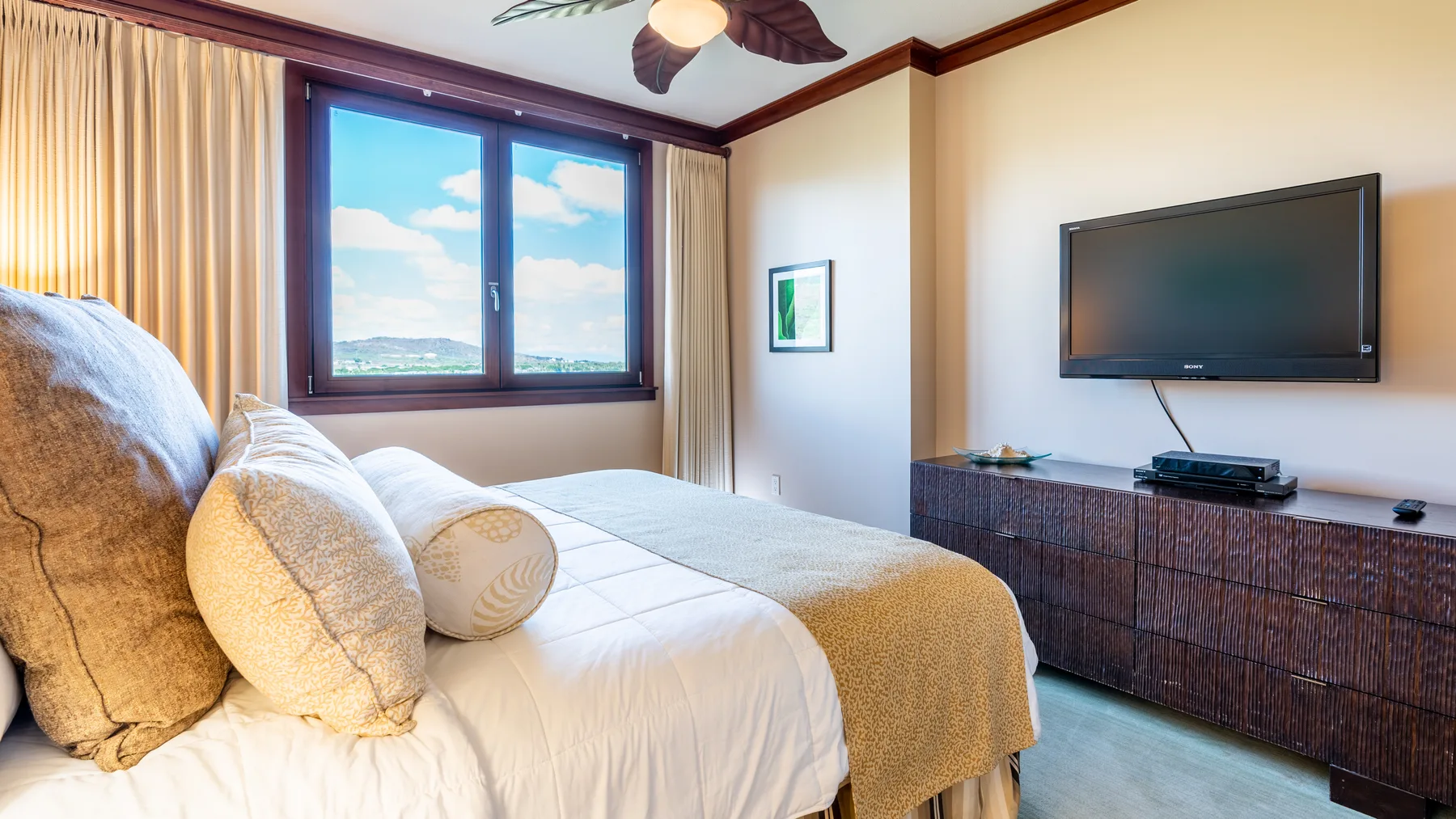 A bedroom with a bed beside a window and a television mounted above a dresser.