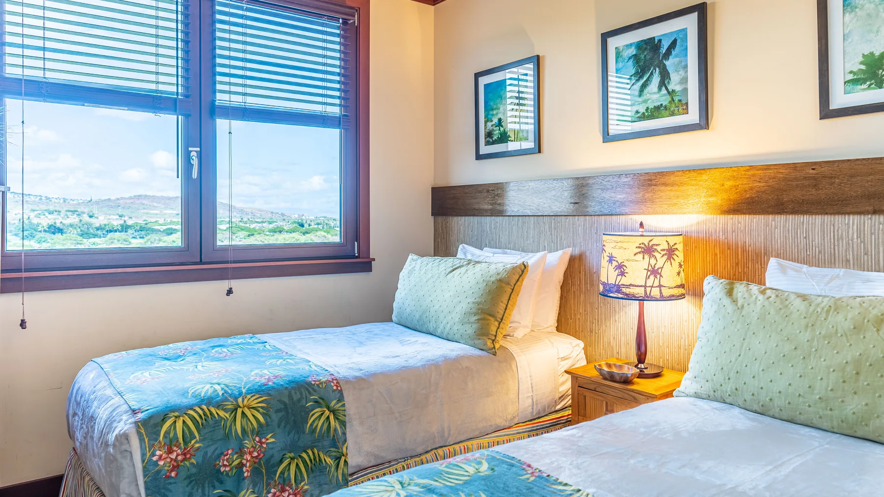 A bedroom with two beds, patterned bedding, and windows overlooking a green landscape.