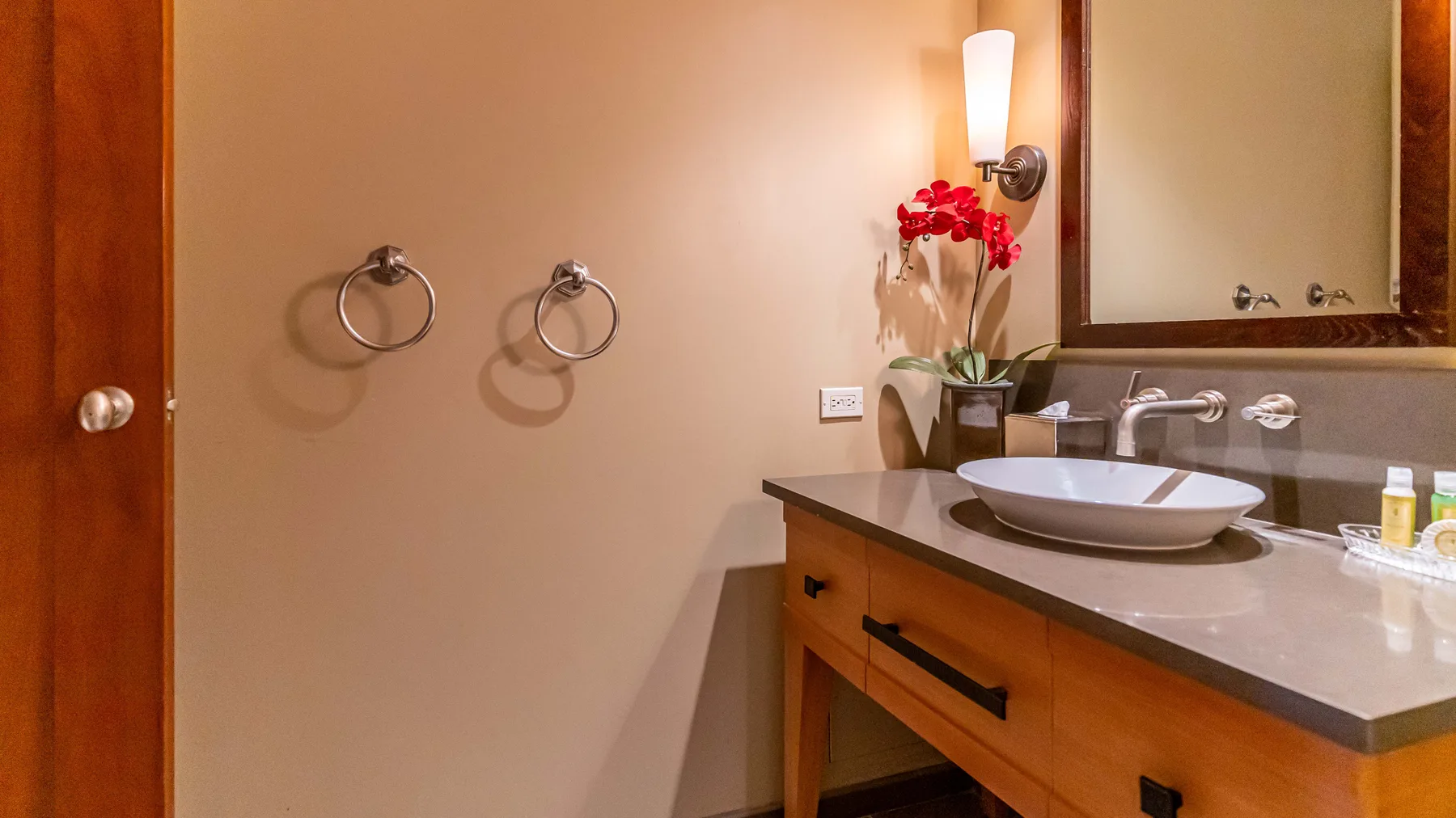 A bathroom vanity with a basin, mirror, and red flowers.